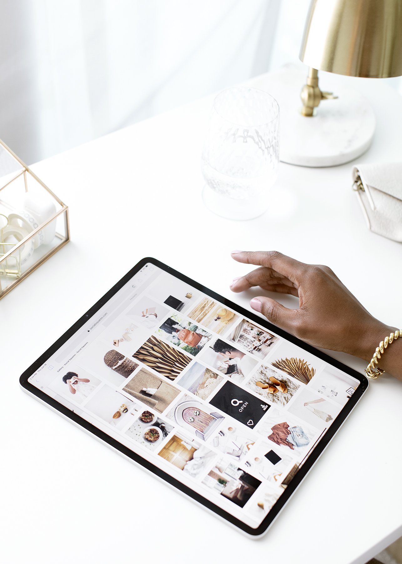 A woman's hand next to a black iPad on a white desk with white and gold accessories